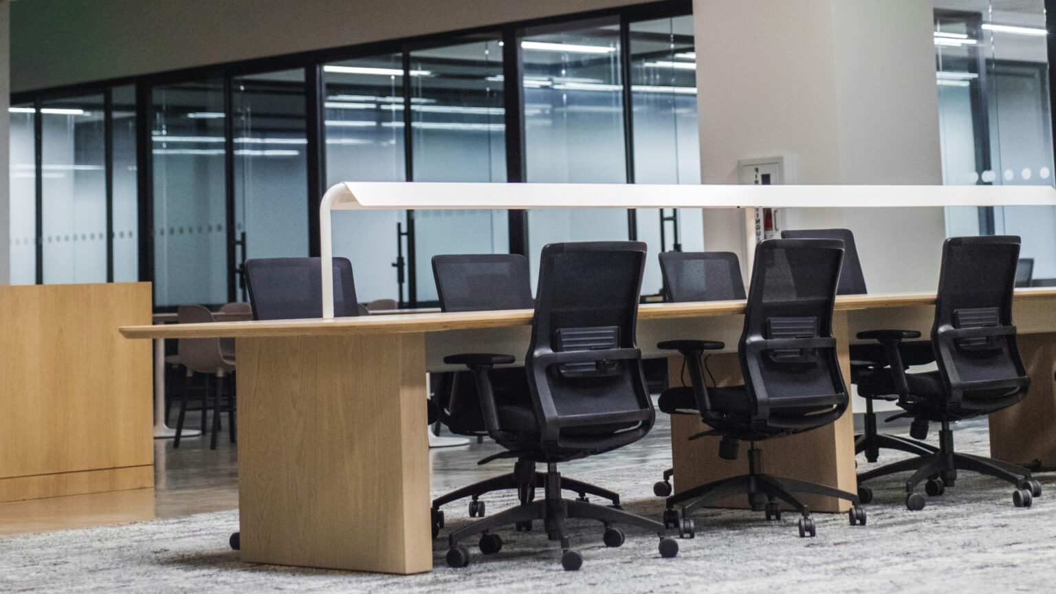 General contractor in Turtle Bay. Modern open-concept office workspace with ergonomic black mesh chairs, a shared wood workstation, built-in task lighting, and floor-to-ceiling glass partitions for a clean, collaborative, and professional environment.