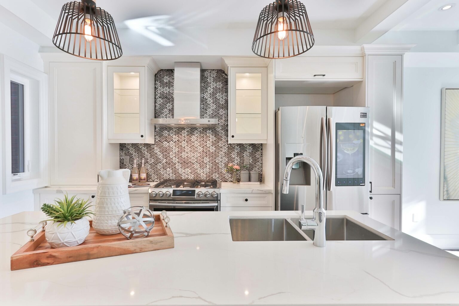 Contemporary white kitchen with quartz countertops, dual-basin sink, stainless steel appliances, decorative mosaic tile backsplash, glass-front cabinets, and modern pendant lighting, designed for both elegance and functionality.