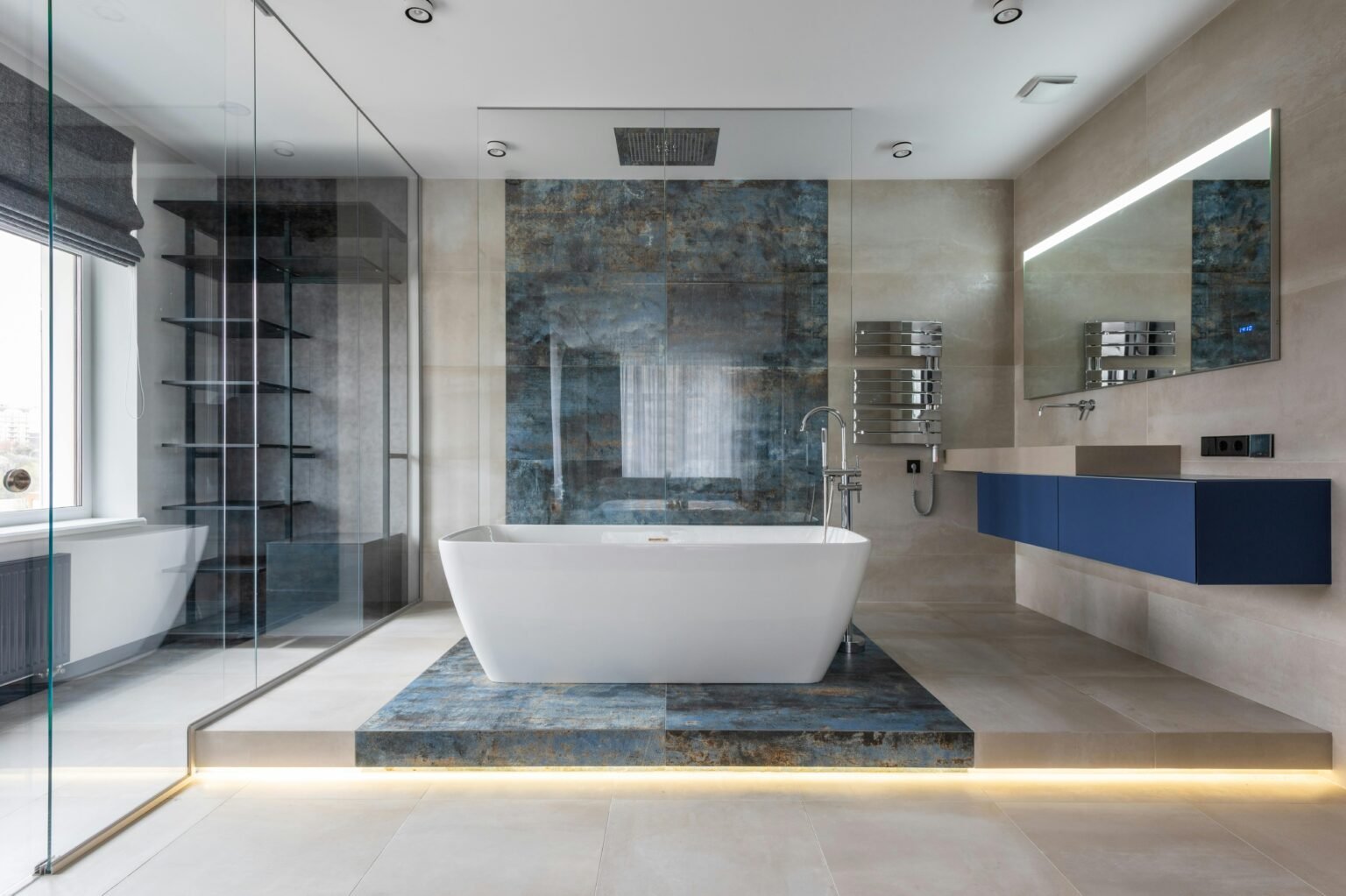 Luxurious modern bathroom featuring a freestanding soaking tub on a raised marble platform, surrounded by large beige tiles, a glass-enclosed rainfall shower, floating blue vanity with underlit mirror, and sleek chrome fixtures, showcasing high-end contemporary remodeling design.