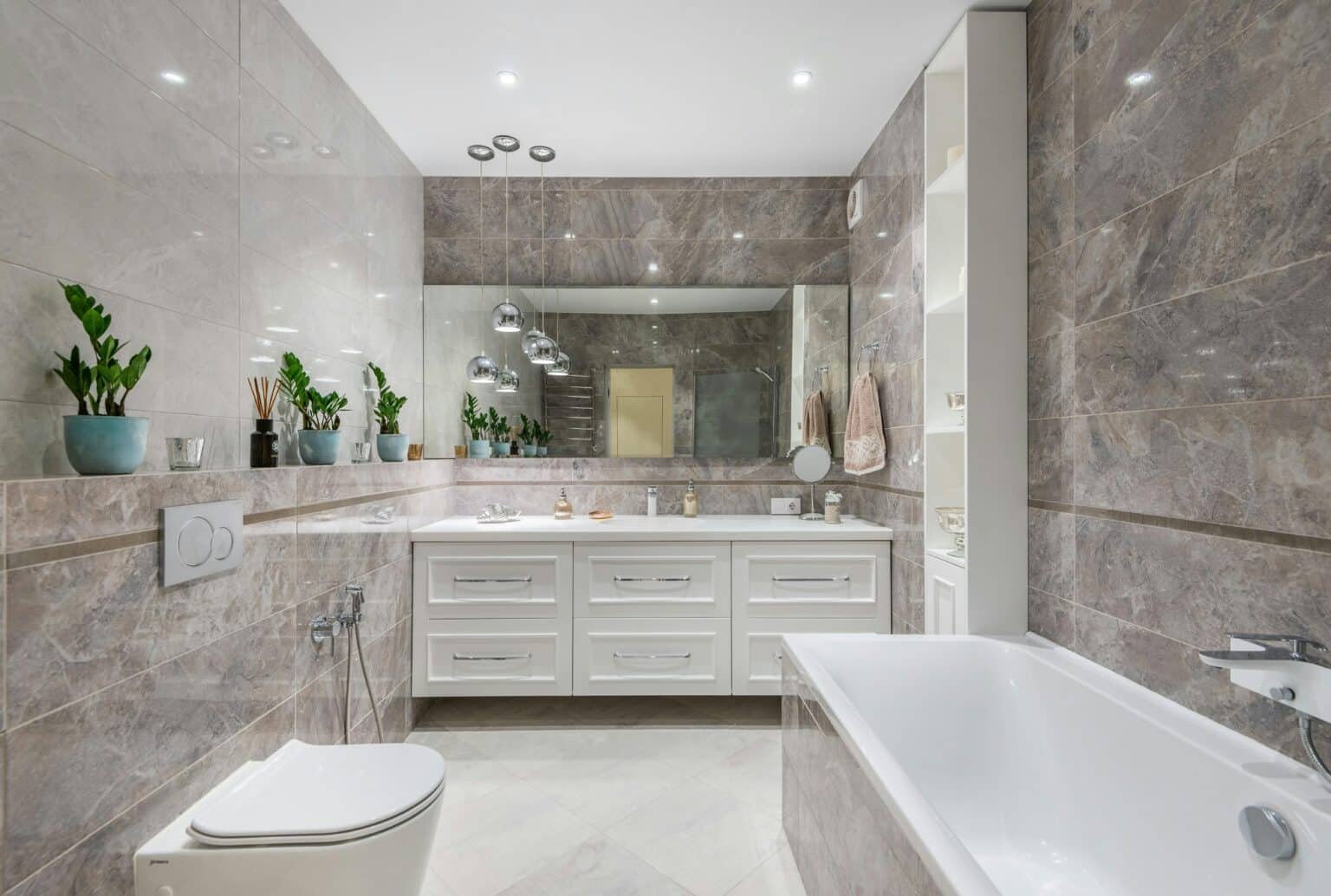 Spacious contemporary bathroom with glossy marble-look wall tiles, a large white double-sink vanity with chrome hardware, and a built-in bathtub. The space features modern pendant lighting, a wide mirror, open shelving with neatly arranged towels and decor, and potted greenery for a fresh, serene atmosphere.